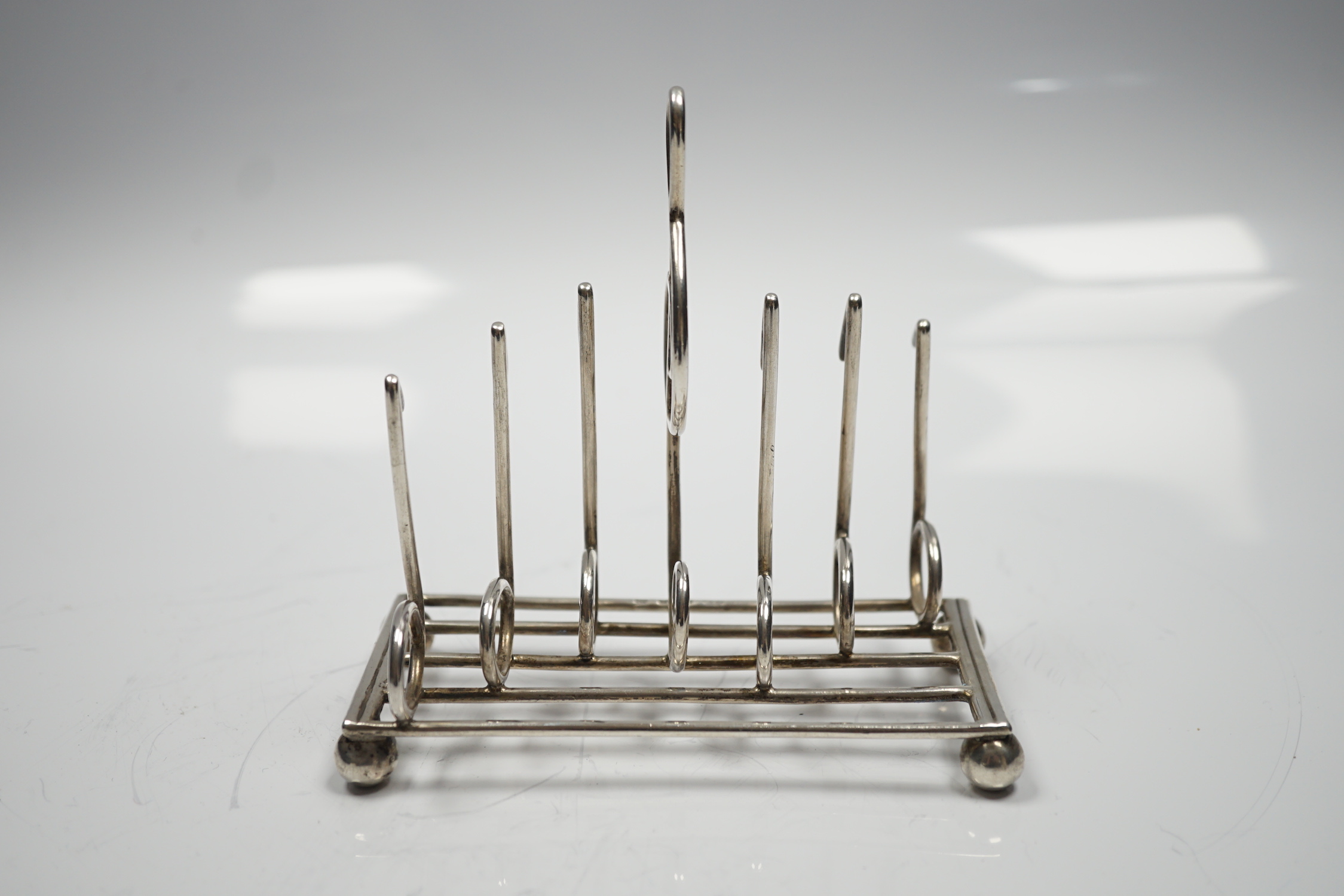 A late Victorian novelty silver toast rack, the dividers modelled as musical notes, with central handle modelled as a treble clef, on ball feet, Norton & White, Birmingham, 1898, length 12.5cm, 139 grams.